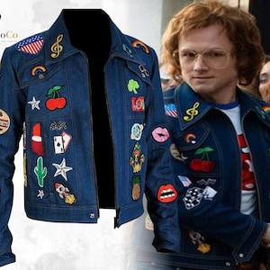 May include: A dark blue denim jacket featuring a variety of colourful embroidered patches including cherries, a rocket, a cactus, a pineapple, lips, playing cards, stars, rainbows, and an American flag, with a classic collar and front button closure.