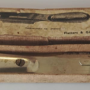 Könnte beinhalten: Ein vintage Mikrops Sektionsmesser mit Metallgriff und Klinge, untergebracht in einer rechteckigen Pappschachtel. Der Deckel trägt den Text The Mikrops Section Knife, Made in England, und Flatters & Garnett Ltd, Manchester.