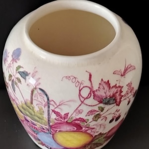 May include: A cream-colored ceramic vase with a rounded shape and a wide opening. The exterior features a detailed botanical illustration in shades of pink, yellow, green, and blue, depicting various fruits, leaves, and delicate vine tendrils.