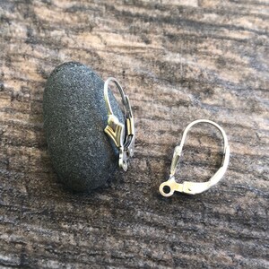 May include: Two silver earring hooks, one on a gray stone and one on a wooden surface.