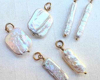 May include: Five irregularly shaped, white freshwater pearl pendants with gold-colored findings. The pearls vary in shape, including rectangular and oblong, and have a lustrous, iridescent sheen. Each pendant has a small gold bead at the bottom.