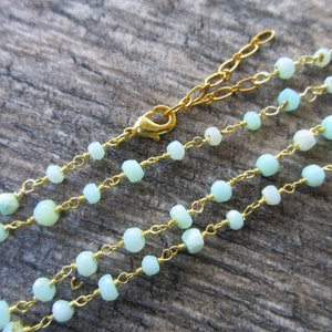 May include: A delicate gold chain necklace with light blue opal beads. The necklace has a lobster clasp closure.