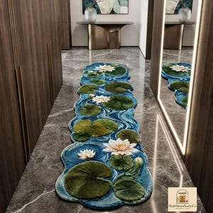 May include: A long, irregularly shaped runner rug featuring a pond-inspired design with deep blue swirling water patterns, vibrant green lily pads, and white lotus flowers in various stages of bloom, laid out on a dark gray marble floor.