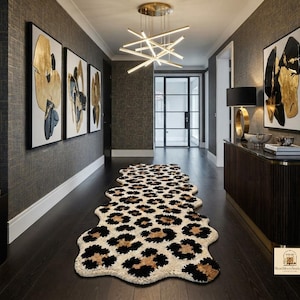 Peut inclure: Un long tapis de forme irrégulière présentant un motif léopard répétitif dans des tons noir, beige et crème. Le tapis est placé au centre sur un sol en bois sombre dans un couloir, mettant en valeur une surface texturée à poils longs.