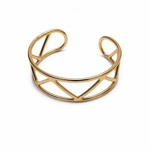 Può includere: Un bracciale a fascia in metallo color oro caratterizzato da un design traforato composto da forme triangolari interconnesse. Il bracciale presenta una struttura circolare con un'apertura sul retro, una finitura lucida e un motivo geometrico.