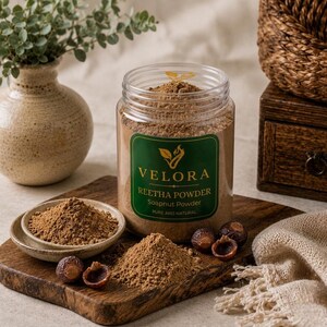 Könnte beinhalten: Ein durchsichtiger Kunststoffbehälter gefüllt mit braunem Reetha-Pulver, etikettiert mit Velora Reetha Powder Soapnut Powder Pure and Natural. Neben dem Behälter steht eine kleine Keramikschale mit Pulver, losem Pulver und getrockneten Waschnüssen.