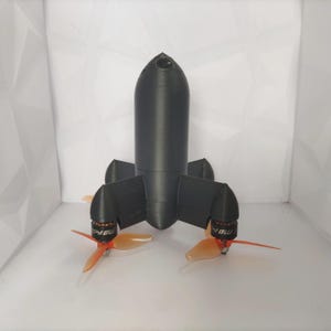 May include: A matte black drone frame with a cylindrical central body and four protruding motor mounts. Each mount features a small black motor labeled MB140 and a three-bladed translucent orange propeller. The structure has a smooth finish.