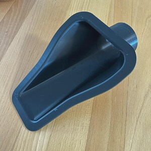 Pode incluir: Um acessório de aspirador de pó em plástico cinza-escuro impresso em 3D, com um bocal de entrada largo de formato triangular que se estreita para uma porta de conexão cilíndrica. O objeto possui um acabamento fosco liso e estrutura rígida.