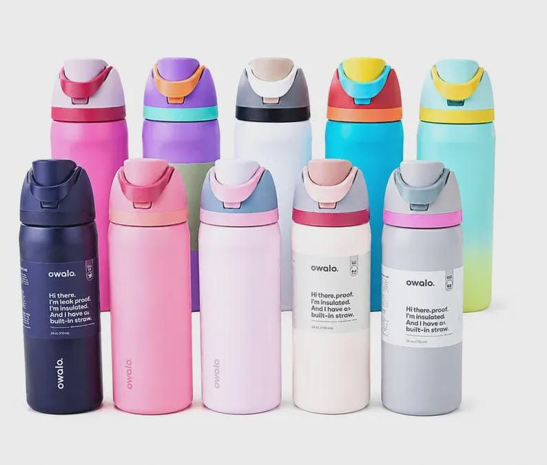 Op de afbeelding: Een collectie van tien ge&iuml;soleerde Owala-waterflessen in diverse kleuren, waaronder roze, blauw, wit en marineblauw. Elke fles heeft een klapdeksel met ingebouwd rietje en een label met een inhoud van 710 ml op de verpakking.