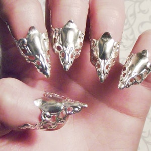 May include: Five silver fingertip rings with a pointed, claw-like design. The rings are made of a delicate, openwork metal and have a shiny finish.