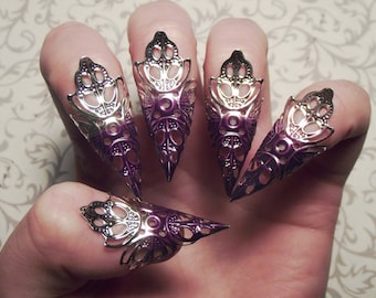 May include: Five silver and purple nail rings with intricate designs. The rings are shaped like claws and have a pointed tip.