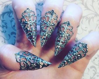 Puede incluir: Cinco anillos de garra de filigrana plateada. Los anillos son puntiagudos y tienen un diseño delicado e intrincado.