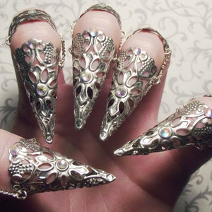 Puede incluir: Conjunto de cinco anillos de dedo de plata con un diseño delicado y ornamentado. Cada anillo presenta un diseño puntiagudo en forma de cono con un patrón de corte y piedras de imitación iridiscentes.