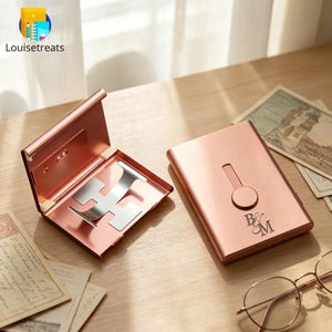 May include: Two rose gold metal card cases with a smooth finish. One case is open, revealing a silver interior clip mechanism. The other case is closed and features a vertical slider and the engraved letters B&M on the front surface.