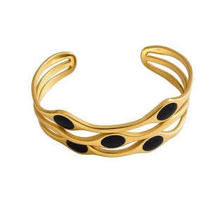 Puede incluir: Una pulsera tipo brazalete de tono dorado con un diseño ondulado de varias capas. La estructura consta de tres bandas interconectadas con curvas suaves y fluidas. Incrustadas en el metal dorado hay varias piezas negras de forma ovalada.
