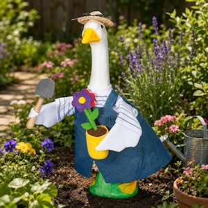 Puede incluir: Una figura de ganso blanco con sombrero de paja, camisa de rayas azules y blancas y un delantal de mezclilla azul. El ganso sostiene una pequeña paleta de jardín gris en un ala y una maceta amarilla con una flor morada en la otra.
