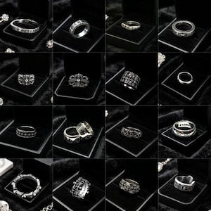 May include: A collection of sixteen silver rings displayed in individual black jewelry boxes. Each ring features intricate metalwork, including cross motifs, engraved lettering, and ornate patterns, showcasing a variety of band styles.