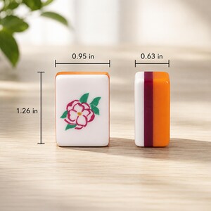 K&ouml;nnte beinhalten: Zwei rechteckige Mahjong-Spielsteine mit den Ma&szlig;en 2,41 cm Breite, 1,60 cm Tiefe und 3,20 cm H&ouml;he. Ein Stein hat eine wei&szlig;e Vorderseite mit einer rosa-gr&uuml;nen Blumenillustration, der andere zeigt ein Seitenprofil mit orangefarbenen und kastanienbraunen Schichten.