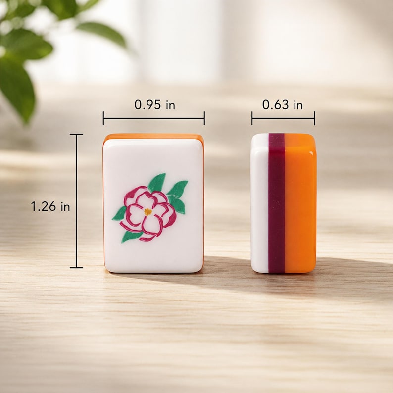 K&ouml;nnte beinhalten: Zwei rechteckige Mahjong-Spielsteine mit den Ma&szlig;en 2,41 cm Breite, 1,60 cm Tiefe und 3,20 cm H&ouml;he. Ein Stein hat eine wei&szlig;e Vorderseite mit einer rosa-gr&uuml;nen Blumenillustration, der andere zeigt ein Seitenprofil mit orangefarbenen und kastanienbraunen Schichten.