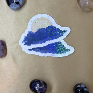 Könnte beinhalten: Zwei gestanzte Aufkleber in Form einer dunkelblauen Wolke mit holografischem Glitzereffekt. Der obere Aufkleber zeigt einen blassgelben, kreisförmigen Mond, der teilweise von der Wolke verdeckt wird. Beide Aufkleber haben einen weißen Rand.