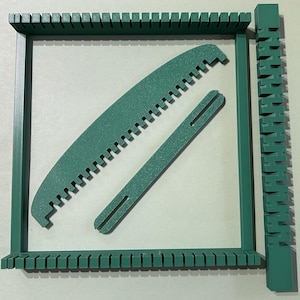 May include: A dark green weaving loom kit consisting of a rectangular frame with notched edges, a curved shed stick with teeth, a straight slotted bar, and a long vertical piece with interlocking notches along its entire length.
