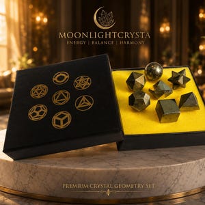 Op de afbeelding: Een zwarte doos met gouden geometrische symbolen en de tekst MOONLIGHTCRYSTA ENERGY | BALANCE | HARMONY met metalen veelvlakken en een bol op een felgeel schuimrubberen inzetstuk, gelabeld PREMIUM CRYSTAL GEOMETRY SET.