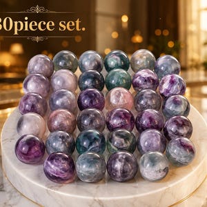Può includere: Un set di 30 pietre sferiche levigate nei toni del viola, verde e bianco, disposte a griglia su un espositore circolare in marmo bianco. Il testo 30piece set. è visibile nell'angolo in alto a sinistra dell'immagine.