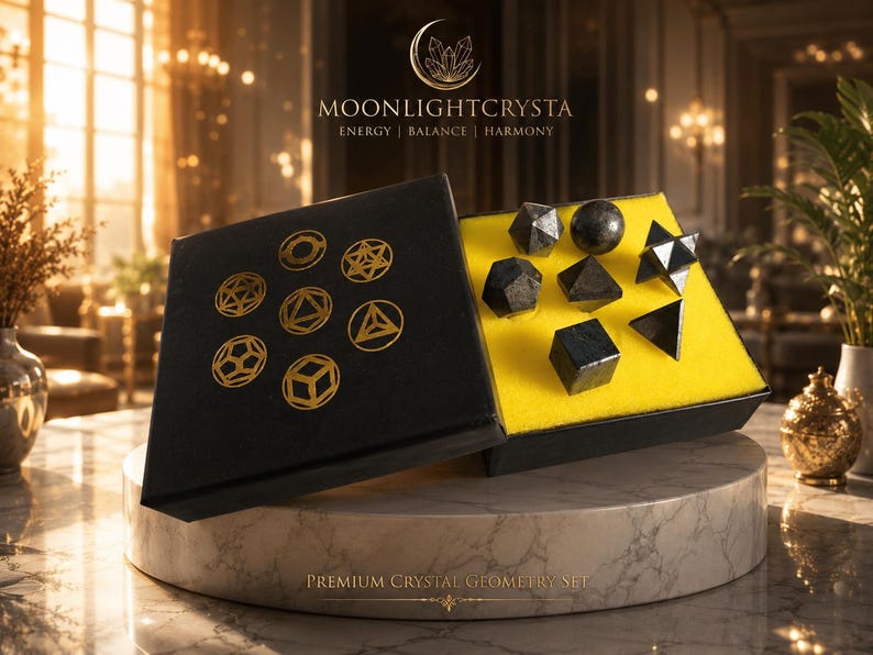Op de afbeelding: Een zwarte doos met zeven donkere, gepolijste geometrische kristalvormen in felgeel schuim. Het deksel bevat goudkleurige lijntekeningen van diverse veelvlakken en de tekst MOONLIGHTCRYSTA ENERGY | BALANCE | HARMONY.