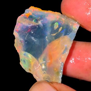 Könnte beinhalten: Ein roher, durchscheinender Opal mit unregelmäßiger Form, der ein lebhaftes Farbspiel mit roten, orangen, grünen und blauen Blitzen auf seiner Oberfläche zeigt. Der Stein hat ein glattes, poliertes Aussehen und eine helle, milchige Basis.