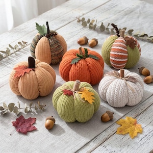 May include: A collection of six fabric pumpkins in various colors including orange, green, white, and tan, featuring ribbed knit textures. Each pumpkin is topped with a stem and decorated with small fabric leaves, twine, or curled wire accents.