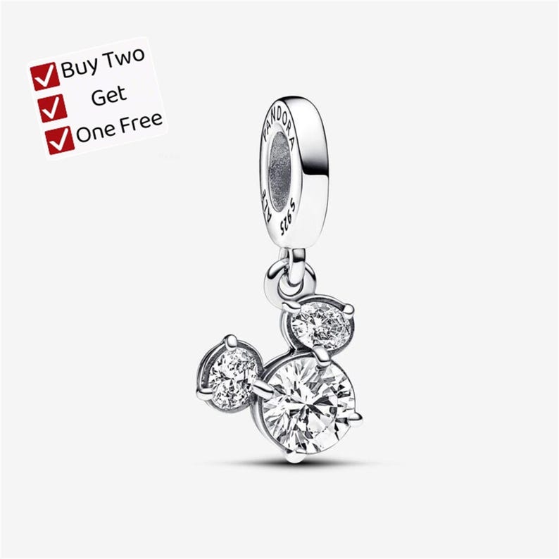 May include: A silver dangle charm featuring three round clear stones arranged in a cluster, with the text PANDORA S925 engraved on the bail. A white square graphic in the corner displays the text Buy Two Get One Free with three red checkmarks.