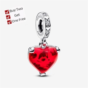 May include: A silver charm featuring a bright red heart pendant suspended from a circular bail. The bail is engraved with the text Pandora and Disney, and is accented with small clear stones. A white label displays the text Buy Two Get One Free.