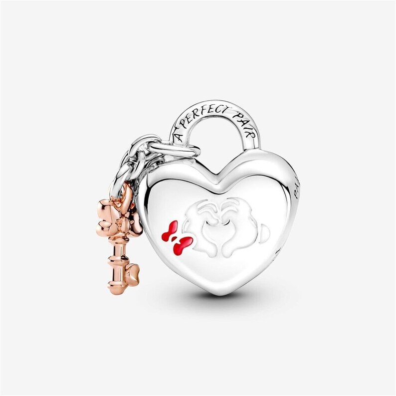 May include: A silver heart-shaped padlock charm featuring the engraved text A PERFECT PAIR on the shackle. The front displays white cartoon gloved hands forming a heart shape with a small red bow. A rose gold-toned key charm hangs from the side.