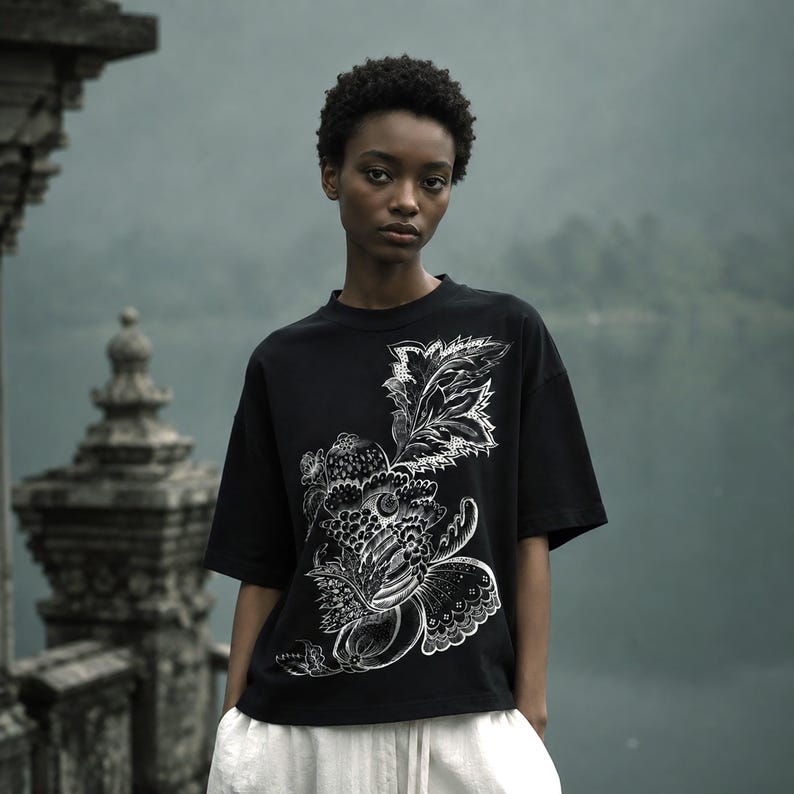 Pu&ograve; includere: Una t-shirt nera a maniche corte con una dettagliata stampa grafica bianca di elementi botanici stilizzati, tra cui foglie, fiori e forme simili a frutti, disposti in un motivo asimmetrico sulla parte anteriore del capo.