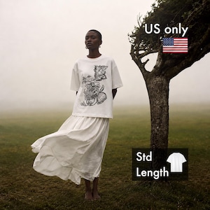 Pu&ograve; includere: Una t-shirt bianca a maniche corte con un'illustrazione botanica nera sul petto, abbinata a una gonna bianca lunga e fluida. La maglietta ha una lunghezza standard e il testo US only &egrave; visibile nell'angolo in alto a destra dell'immagine.