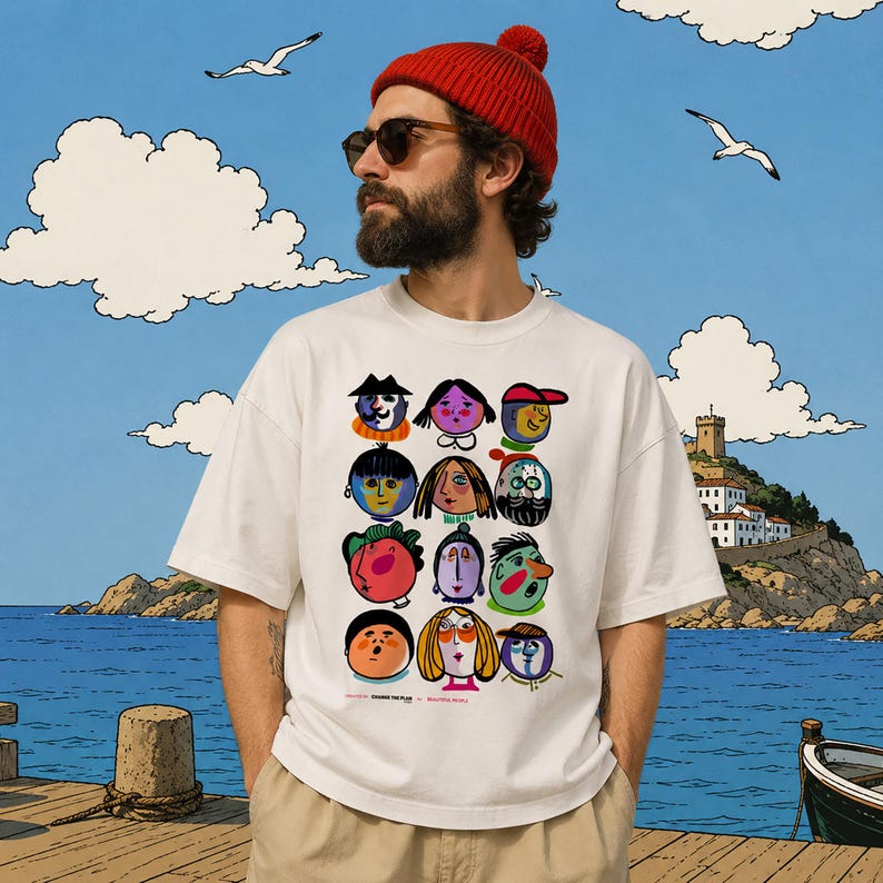 May include: A white short-sleeved t-shirt featuring a graphic print of twelve stylized, colorful cartoon faces arranged in a grid. The design includes small text at the bottom that reads "BEAMING THE PLAN" and "BEAUTIFUL PEOPLE" in a simple black font.