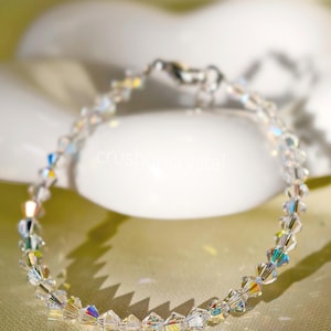 May include: A delicate bracelet composed of clear, faceted bicone crystals that exhibit an iridescent, rainbow-like shimmer. The crystals are strung together in a continuous circular pattern, featuring a metallic clasp closure and the text crushoncrystal.