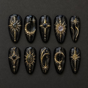 May include: A set of ten almond-shaped press-on nails with a black base featuring gold celestial motifs. Each nail displays unique designs including suns, moons, and stars, accented with small embedded crystals and metallic gold detailing.