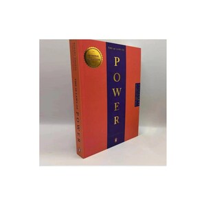 May include: A hardcover book titled The 48 Laws of Power by Robert Greene. The cover is orange with a vertical purple stripe featuring the word POWER in gold lettering. A gold circular seal is on the upper left, and a small penguin logo is at the base.