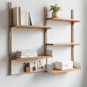 May include: A wall-mounted modular shelving system featuring light wood shelves and white metal uprights. The unit includes a white pegboard section with a small wooden pencil holder, a keychain, and a photo, plus a white storage box on a shelf.