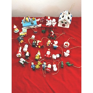 Könnte beinhalten: Eine Sammlung kleiner, handbemalter Weihnachtsanhänger aus Holz mit verschiedenen Figuren wie Schneemännern, Weihnachtsmann, Spielzeugsoldaten, Tieren, einem Haus und einem Schlitten, jeweils mit einer goldenen Schnur zum Aufhängen.
