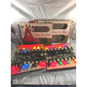 以下が含まれることがあります： マルチカラーの電球が付いた15個の屋内用クリスマスツリーライトの箱が2つ。パッケージは赤と白のデザインで、15 INDOOR LIGHTSおよびChristmas Tree Lightsという文字が記載されています。セットには、赤、青、緑、黄色の電球が付いた黒いコードが含まれています。