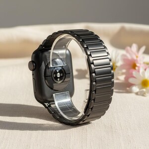 May include: A matte black smartwatch featuring a matching link bracelet band. The device is shown from the rear, displaying the circular sensor array on the back casing. The watch is held in a circular position by a clear plastic display stand.