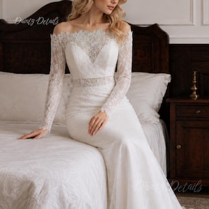 May include: A white floor-length gown featuring long sleeves and an off-the-shoulder neckline. The bodice and sleeves are crafted from intricate floral lace, transitioning into a solid white skirt. The text Dainty Details is visible in the corner.