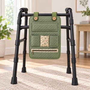Könnte beinhalten: Ein schwarzer Metall-Rollator mit einer gesteppten, olivgrünen Stofftasche an der vorderen Stange. Die Tasche verfügt über zwei Knopfverschlüsse oben, ein horizontales Fach, drei kleinere Vordertaschen und ein Reißverschlussfach mit Blumenmuster.