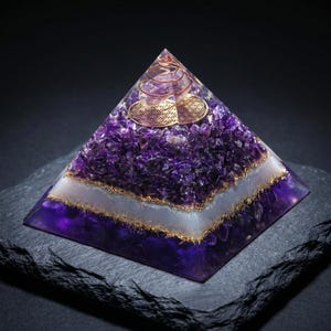 May include: A pyramid-shaped resin object containing deep purple amethyst crystal chips, a horizontal white band, and a gold-colored metal coil at the apex. A circular gold-colored metal plate with a geometric flower of life pattern is embedded near the top.