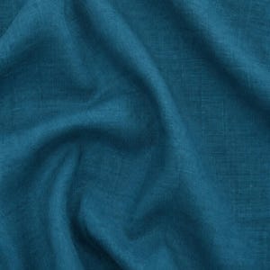 Puede incluir: Una pieza de tela de color verde azulado con una textura tejida visible. El material est&aacute; etiquetado como 10 Harbor Teal 180G Tencel-Linen Fabric. El textil est&aacute; drapeado para crear pliegues suaves y sombras en la superficie del material.