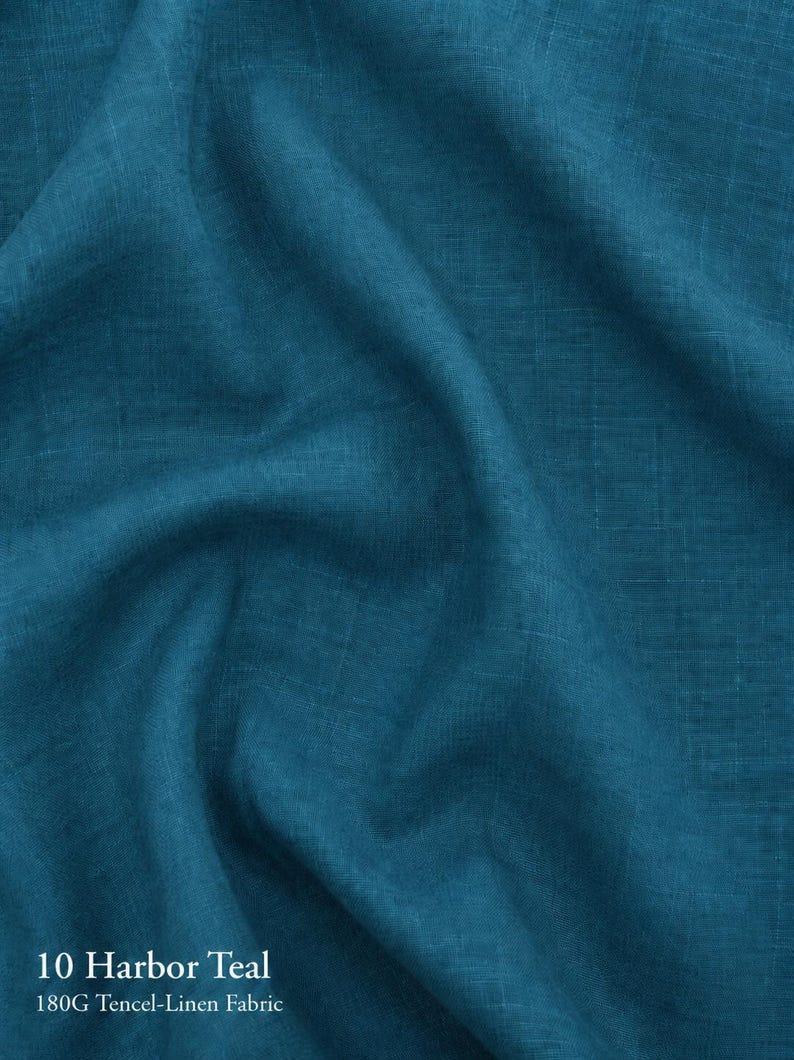 Puede incluir: Una pieza de tela de color verde azulado con una textura tejida visible. El material est&aacute; etiquetado como 10 Harbor Teal 180G Tencel-Linen Fabric. El textil est&aacute; drapeado para crear pliegues suaves y sombras en la superficie del material.
