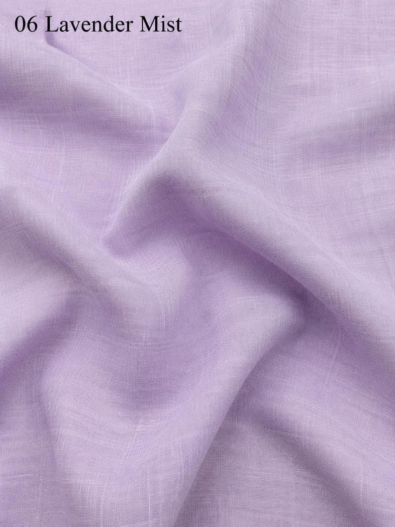 Op de afbeelding: Een lichtpaarse stof met een zichtbare geweven textuur en zachte plooien. De tekst 06 Lavender Mist staat in de linkerbovenhoek gedrukt. Het materiaal vertoont een consistente lavendeltint die het natuurlijke weefsel van het textiel benadrukt.