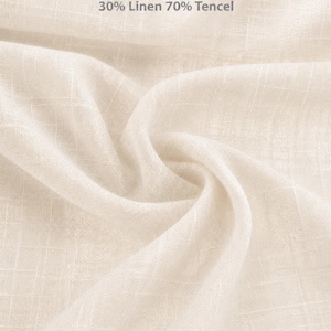 May include: A light beige fabric with a visible weave texture. The text on the fabric reads 125 GSM, 30% Linen 70% Tencel, TENCEL LINEN FABRIC, and Width 57 inch/145 cm. The material is draped to show its soft, lightweight, and semi-sheer quality.